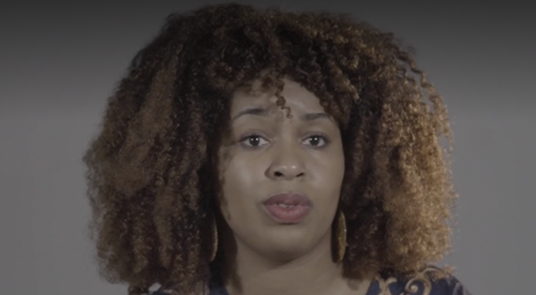 A woman looks past the camera, she is in the midst of speaking