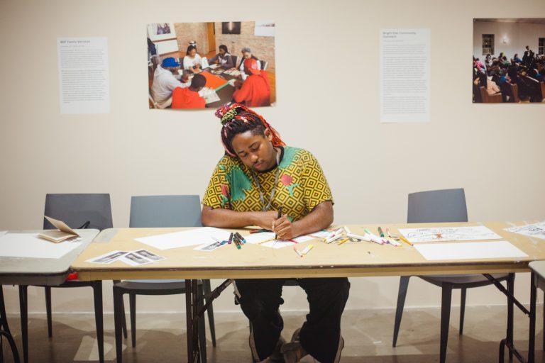 Event participant sitting down and drawing as a part of an Envisioning Justice "Activation Day" workshop.