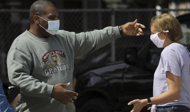 A man wearing a face mask reaches out to hug someone outside the frame of the photo.